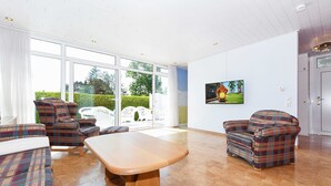 Een ruime kamer met een grote tafel, twee geruite fauteuils en een bank.