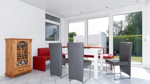 Een eethoek met een witte tafel, rode en grijze stoelen, en een houten kast.