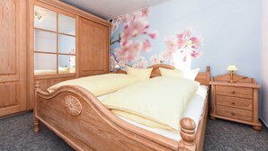 Een houten bed met hoofdbord, een nachtkastje met lamp en een muur met bloemenmotief.