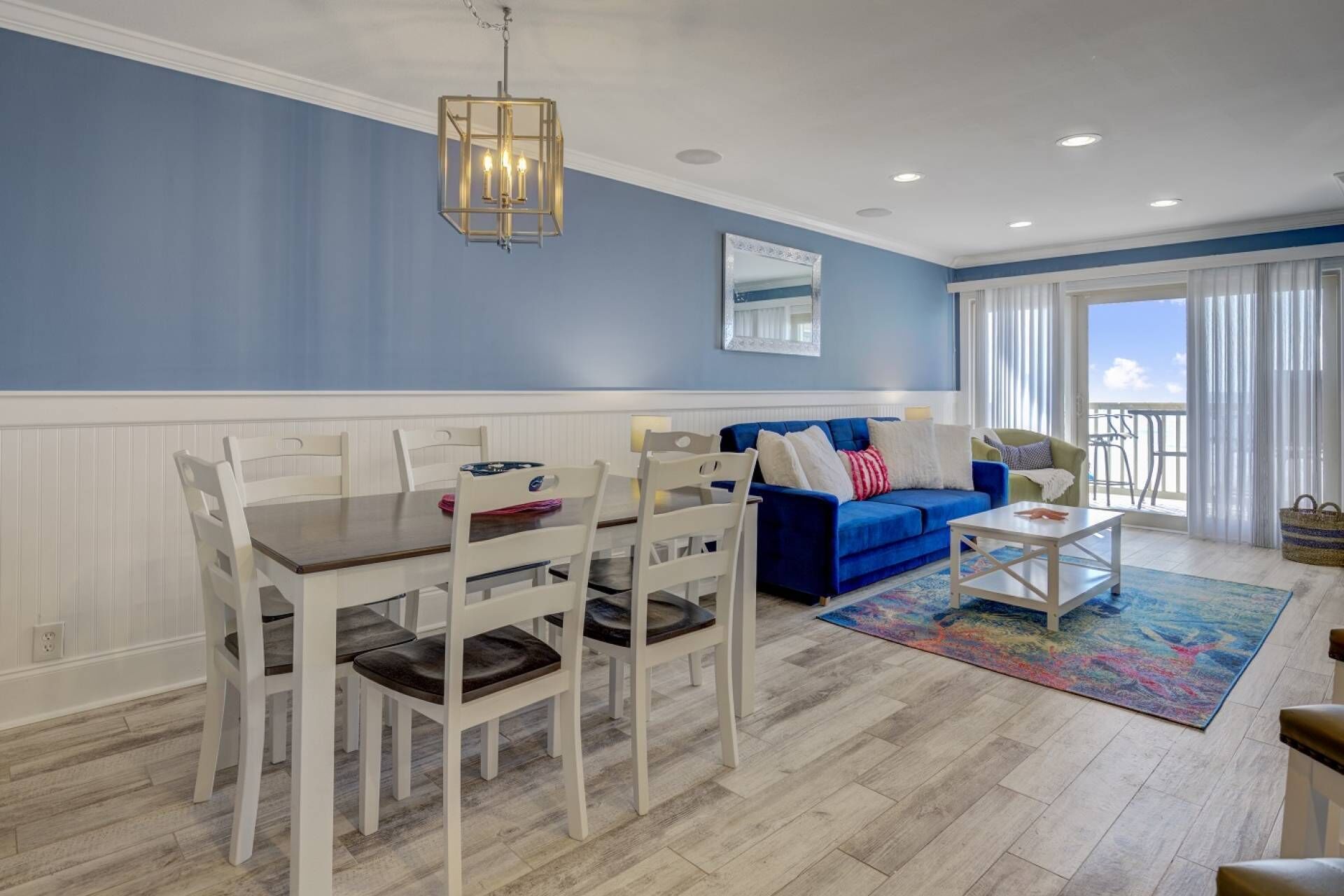 A dining area with a white table and chairs, a blue sofa, and a colorful rug.