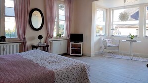 Un dormitorio con cama, televisor, silla y ventana con cortinas.