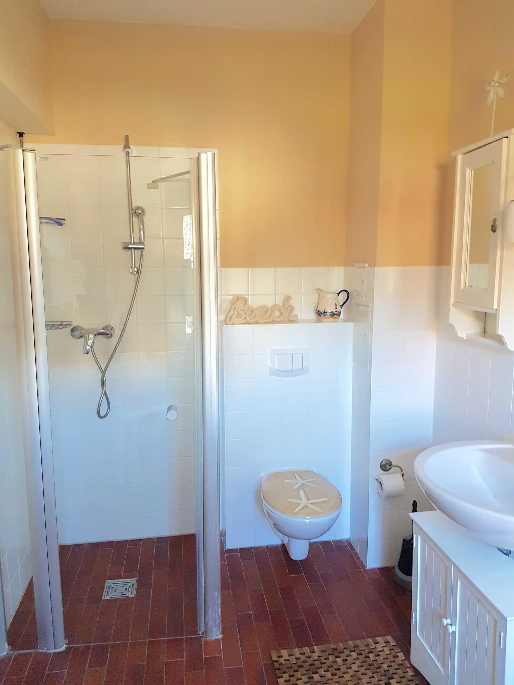 A bathroom with a glass shower enclosure, a toilet, and a sink.