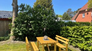 Ein Holztisch mit Bänken in einem Garten, mit Baum und Hecke.