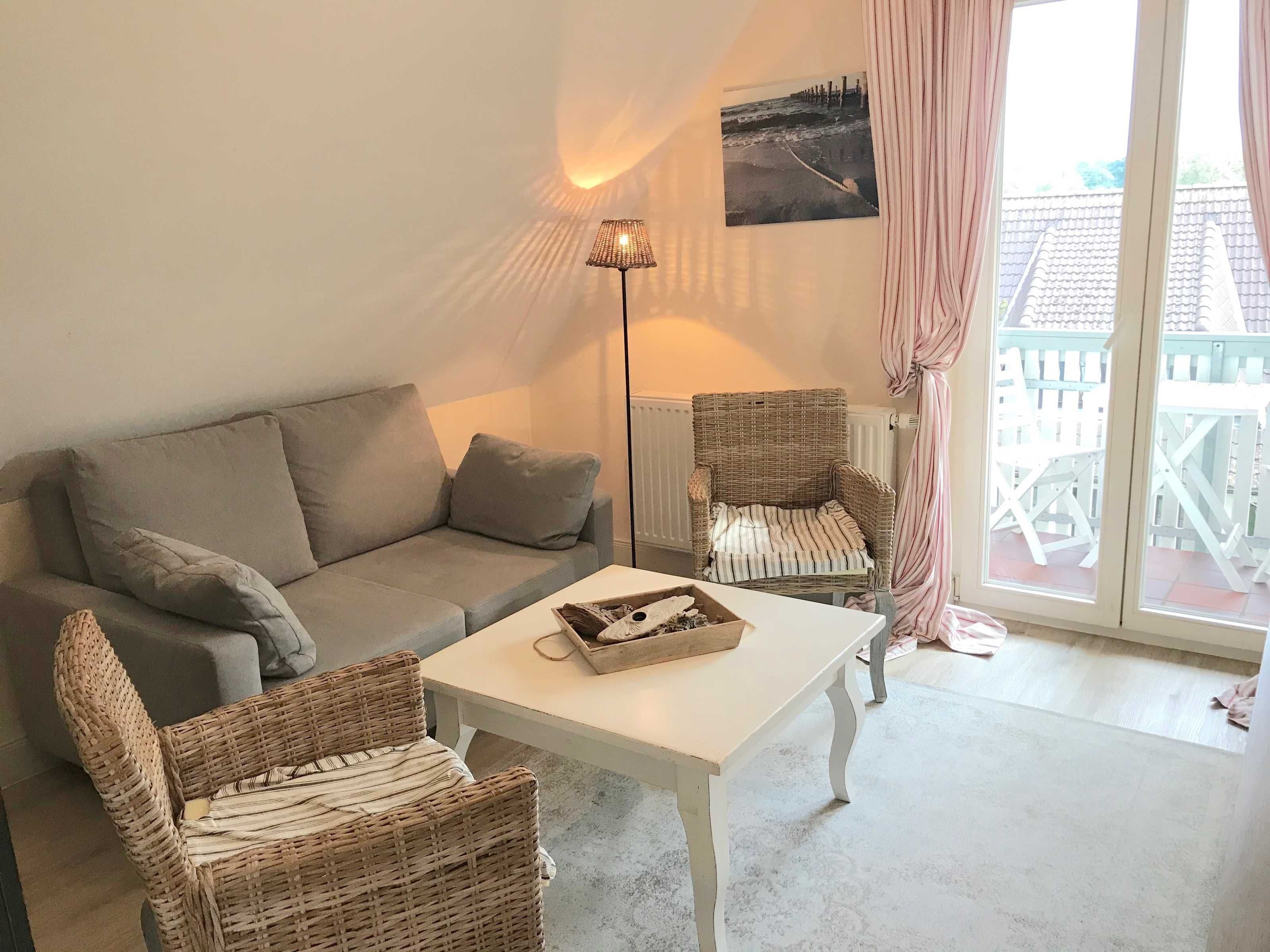 Un salon chaleureux avec un canapé, deux fauteuils en osier, une petite table, une lampe sur pied et une fenêtre avec des rideaux.