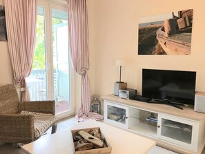 A living room with a television, a white cabinet, a wicker sofa, and a window with curtains. - Ferienwohnung Achterdieck - Haus Borée (Prerow)