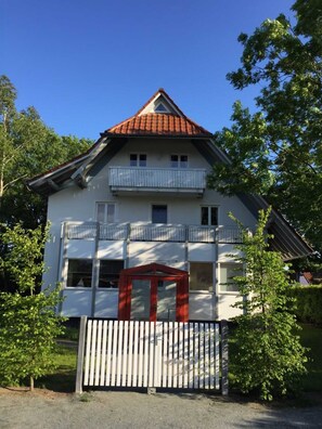 Een gebouw met twee verdiepingen, een rood tegeldak, een balkon op de bovenverdieping en een hekwerk voor de ingang.