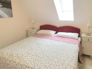Une chambre à coucher avec un lit, deux tables de chevet, une fenêtre et un tableau accroché au mur.