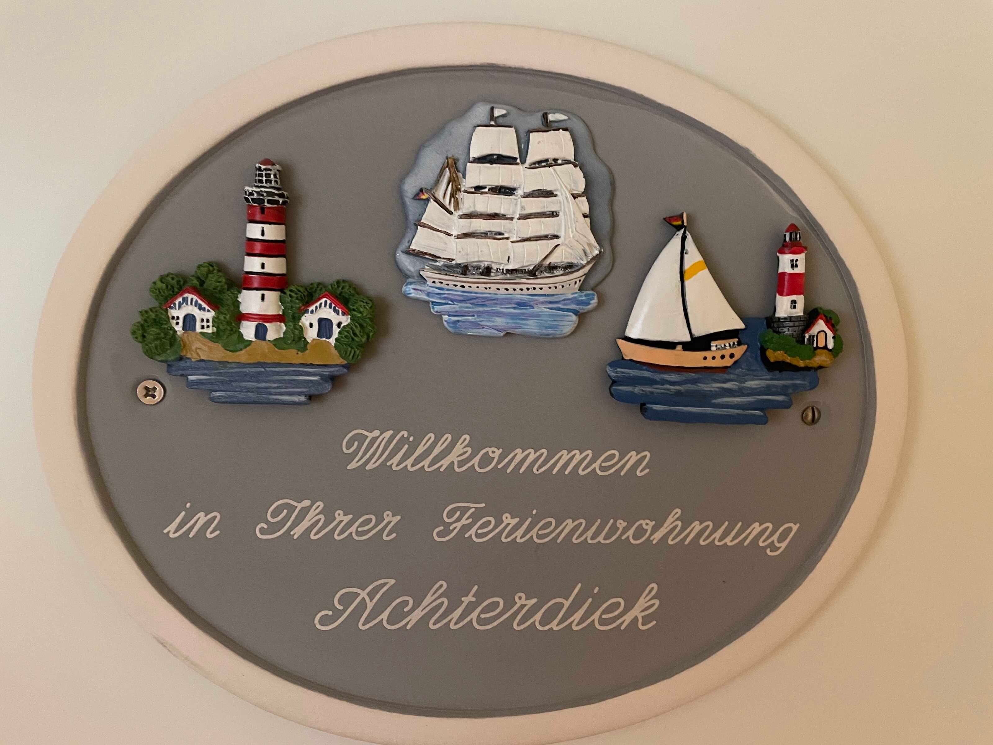 En välkomstskylt med en fyr, en segelbåt och hus.