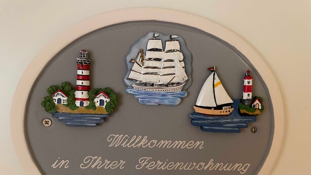 Ein Willkommensschild mit Leuchtturm, Segelboot und Häusern.