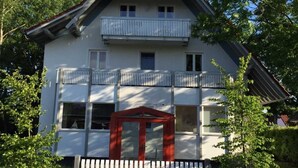 Un bâtiment à deux étages, doté d’un toit recouvert de tuiles rouges, d’un balcon à l’étage supérieur et d’une entrée fermée par un portail.