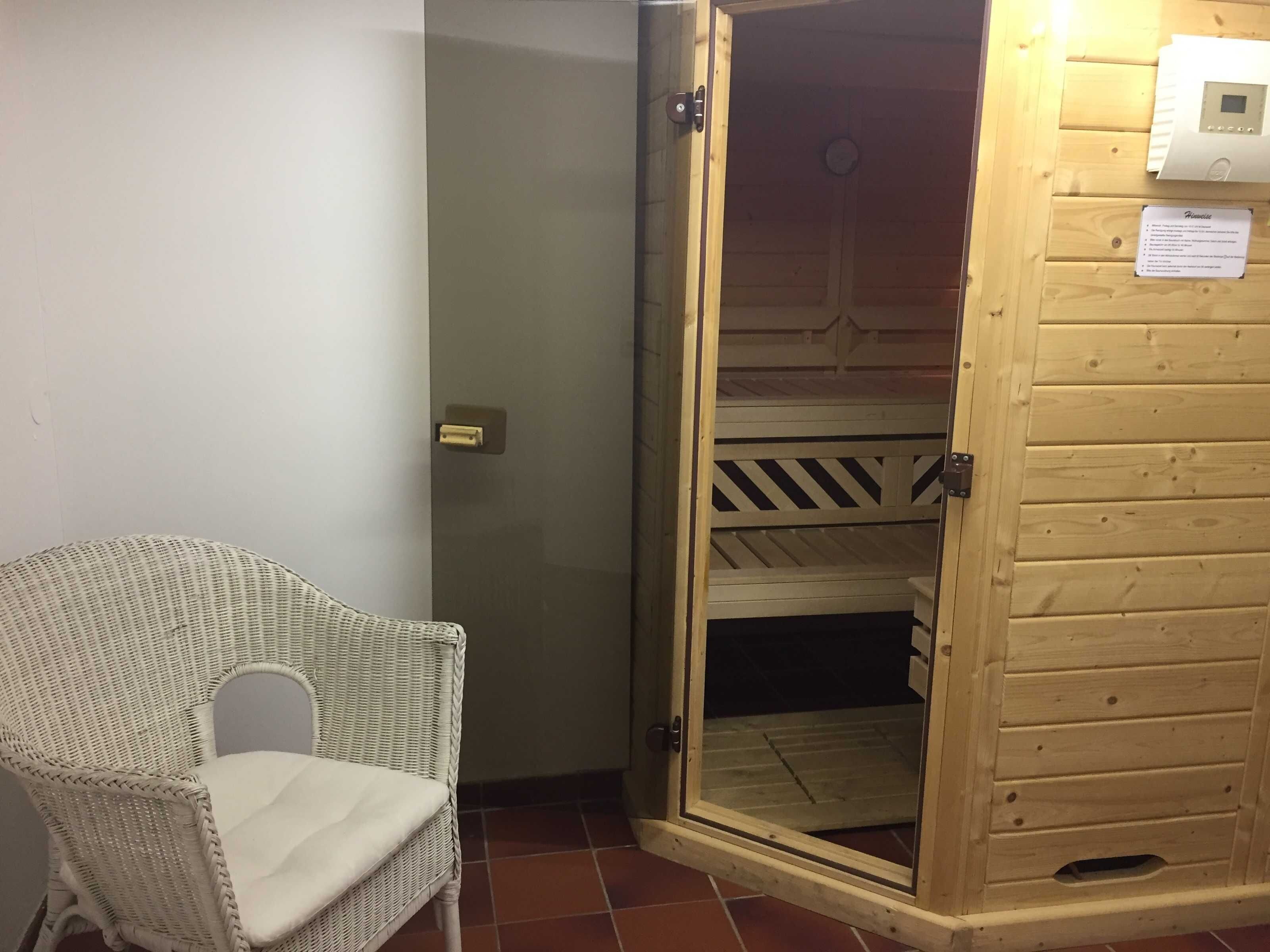 A room with a wicker chair, a wooden bunk bed, and a door with a thermostat on the wall.