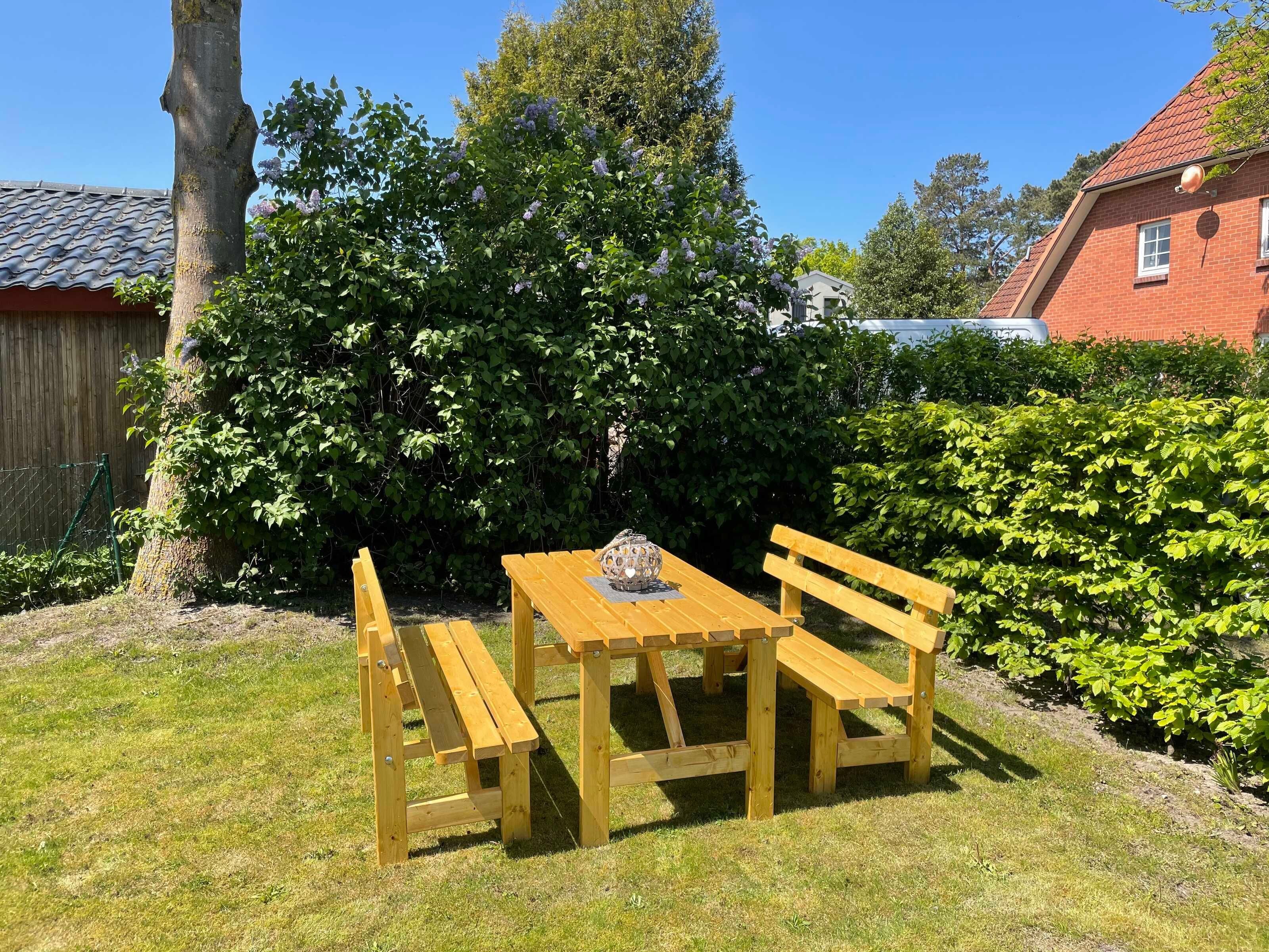 A wooden table and benches in a garden with a tree and a hedge.