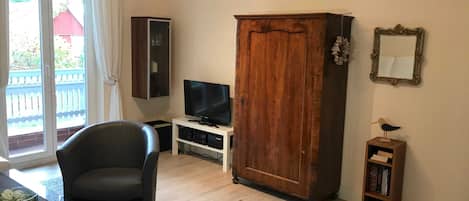A living room with a television, a large wooden cabinet, a bookshelf, and a chair.