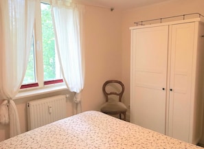 Une chambre à coucher avec un lit, un radiateur, une fenêtre avec des rideaux, une chaise et une armoire.