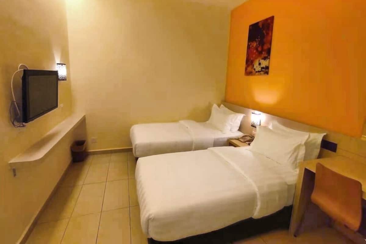 Hotellihuone, jossa on kaksi sänkyä, televisio ja taulu seinällä.