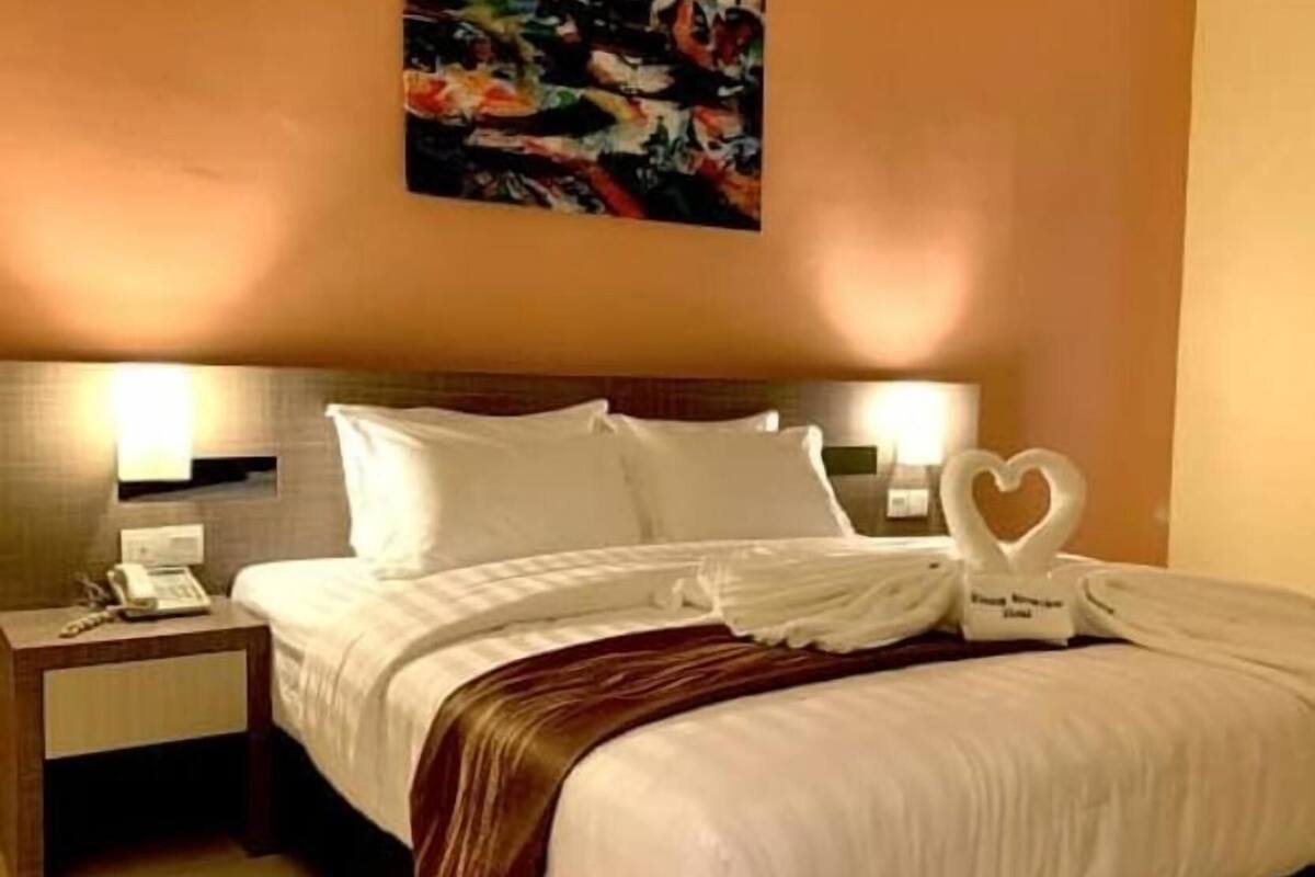 Hotellihuone, jossa on sänky, kaksi yöpöytää, seinälle ripustettu taulu ja sydämenmuotoinen koriste sängyllä.