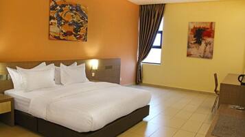 A hotel room with a large bed, a desk, and two paintings on the walls.