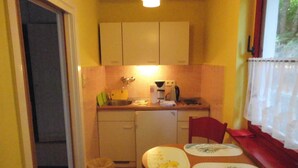 A compact kitchen with basic appliances, a dining table with plates, and a window with curtains. - Ferienwohnung Brandt 45042 We27a - Ferienwohnungen Se-br (Sellin)