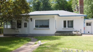 A single-story house with a front porch, a small attached garage, and a brick chimney. - Ferienwohnung Brandt 45042 We27a - Ferienwohnungen Se-br (Sellin)