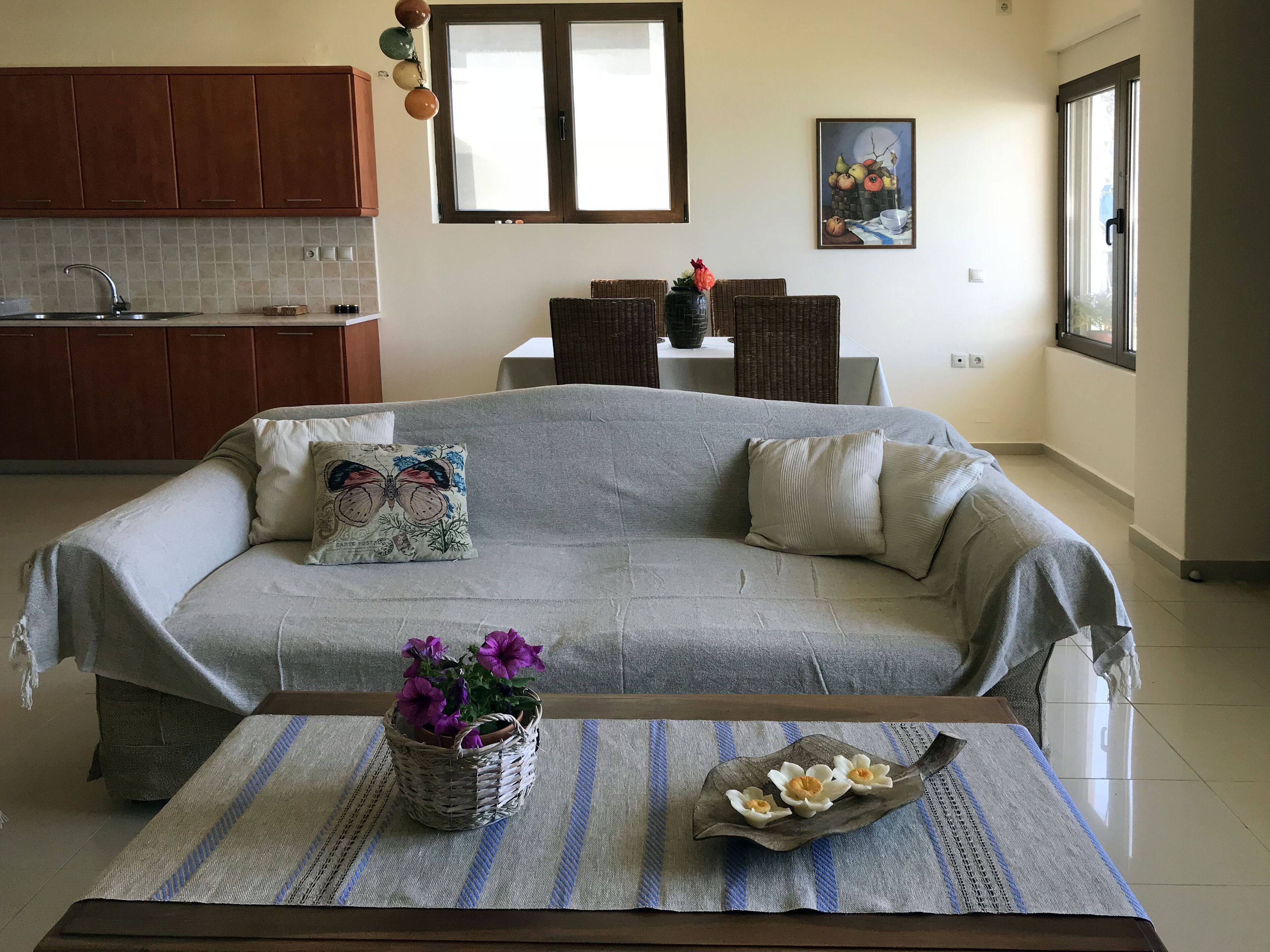 Un área de estar acogedora con un sofá, una mesa de centro con una planta, y una cocina al fondo.