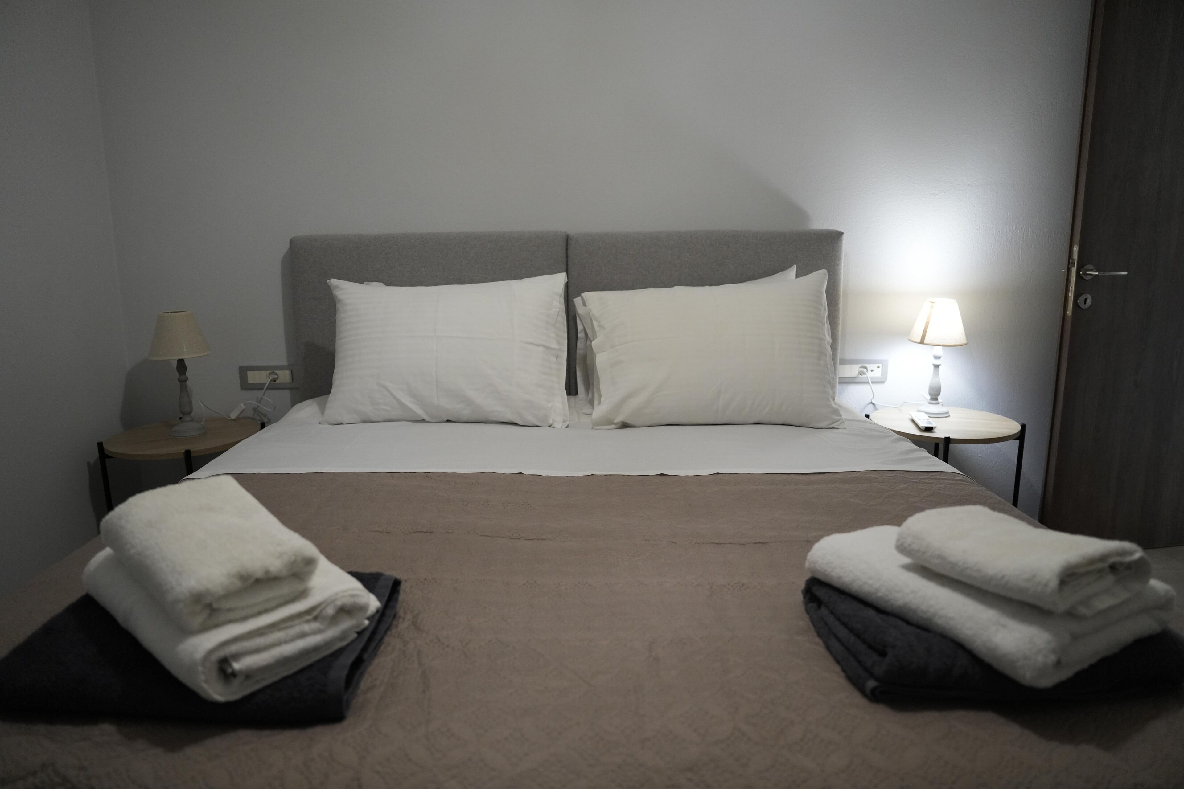 Een hotelkamer met een bed, twee kussens, twee nachtkastjes met lampen en handdoeken op de vloer.
