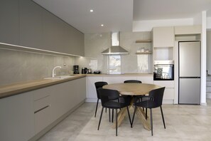 Una cocina moderna con una mesa de comedor de madera y sillas negras, una campana extractora de acero inoxidable y un horno empotrado.