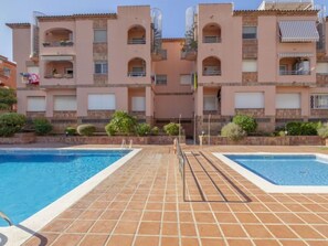 A pool area with two swimming pools, a tiled deck, and a building with multiple balconies. - Torrepuerto by Interhome (Torredembarra)