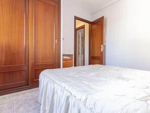 A bedroom with a large wooden wardrobe, a bed with a white bedspread, and a bathroom visible through an open door. - Torrepuerto by Interhome (Torredembarra)