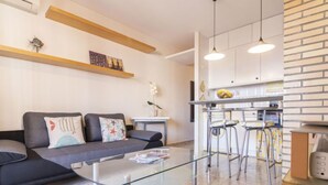 Un soggiorno moderno con un tavolino in vetro, un divano con cuscini decorativi e una zona cucina con sgabelli da bar e una parete a parete rivestita in mattoni.