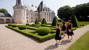 Un bâtiment historique doté d’une tour ronde et d’un jardin à la française avec des haies taillées.