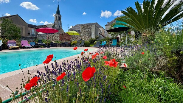 Un espace piscine avec des chaises longues, une église dotée d’un clocher et une grande variété de fleurs.