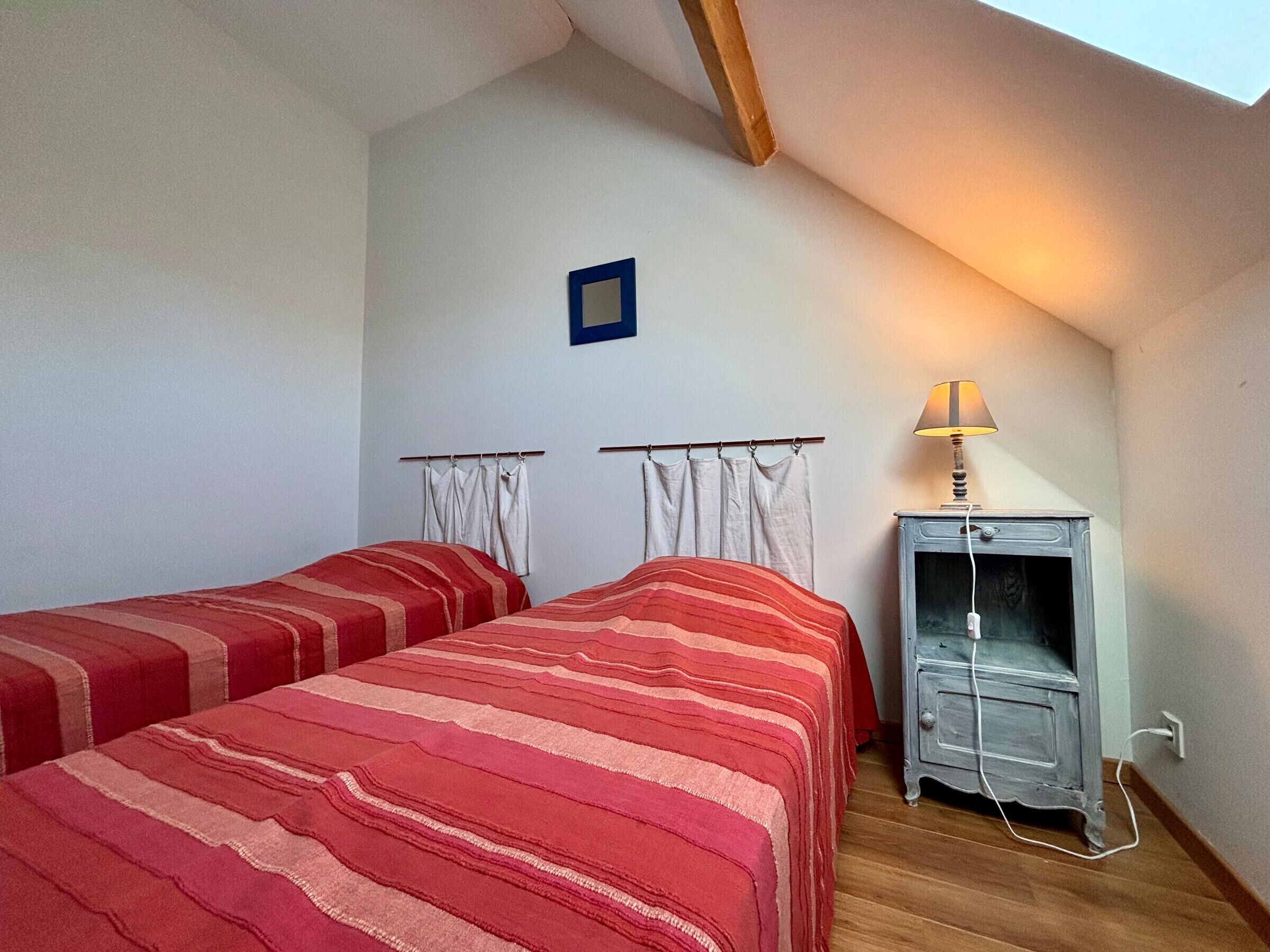 A bedroom with two beds, a nightstand, a lamp, and a picture frame on the wall.