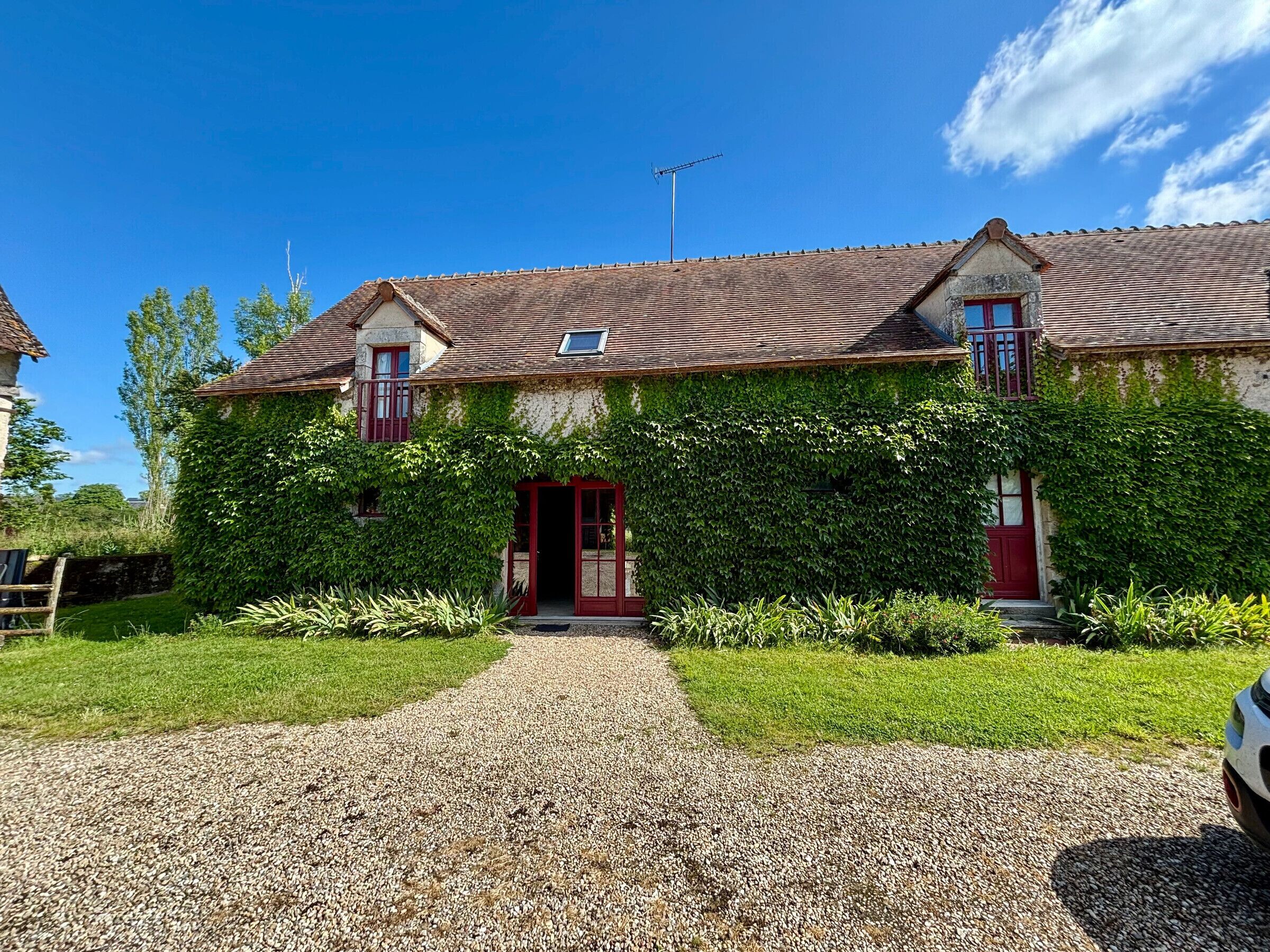 Ein zweistöckiges Haus mit roter Tür, einem Schotterweg und einem Garten mit verschiedenen Pflanzen.
