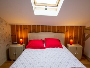 A bedroom with a skylight, a bed with red pillows, two bedside tables with lamps, and wooden paneling on the walls.