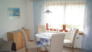 A dining area with a table set for four, surrounded by chairs, a cabinet, and a window with curtains. - Vacation apartment in Seedorf - Holiday apartment Kontschack (Sellin)