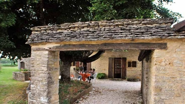 A stone building with a gravel path leading to a covered area with tables and chairs.