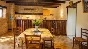 A rustic dining area with a wooden table and chairs, a vase with flowers, and a stone wall in the background.