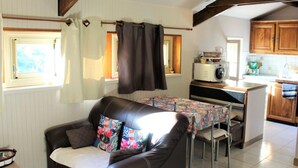 A cozy living room with a leather sofa, a dining table with a floral tablecloth, and a kitchen area with wooden cabinets and a microwave. - Charming studio near Sarlat for a peaceful getaway (La Roque-Gageac)