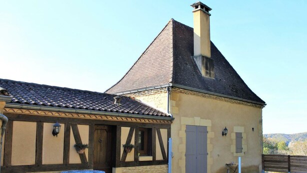 A traditional building with a gabled roof, a chimney, and a small outdoor seating area with a table and chairs. - Charming studio near Sarlat for a peaceful getaway (La Roque-Gageac)