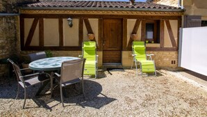 A courtyard with a round table and two green chairs, a wooden door, and a stone wall. - Charming studio near Sarlat for a peaceful getaway (La Roque-Gageac)