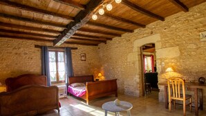 Une pièce rustique avec un plafond en bois, des murs en pierre, un lit recouvert d’une couverture rose, un canapé en bois, une petite table ronde et une chaise.