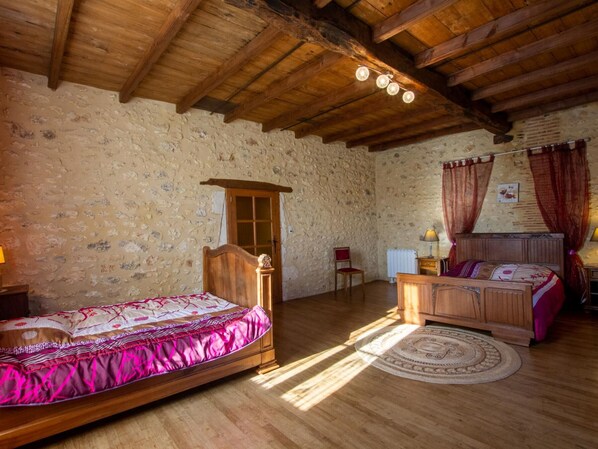 Un dormitorio rústico con pared de piedra, vigas de madera en el techo, una cama con colcha rosa, una mesita de noche de madera y un tapete redondo.