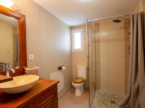 Ein Badezimmer mit einem Holzkosmetikschrank, einem großen Spiegel, einer Toilette und einer gläsernen Duschkabine.