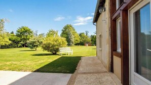 Una casa con entrada pavimentada que lleva a un césped con un banco y un cartel.