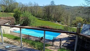 Eine Holzterrasse mit Blick auf ein Schwimmbecken und eine grüne Landschaft mit Bäumen.