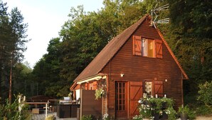 Eine rustikale Holzhütte mit geneigtem Dach, einer Veranda und einer Schotterzufahrt.