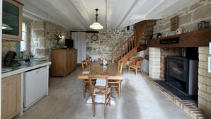 A rustic kitchen with a dining area, stone walls, wooden furniture, and a fireplace.