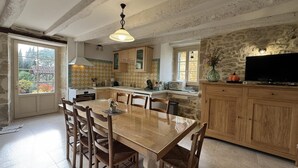A spacious kitchen with a large wooden table and chairs, stone walls, and a stone fireplace.