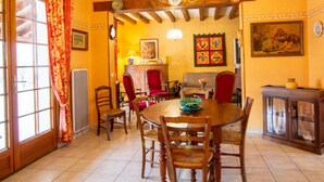 A dining area with a wooden table, chairs, a chandelier, and a view of a kitchen.