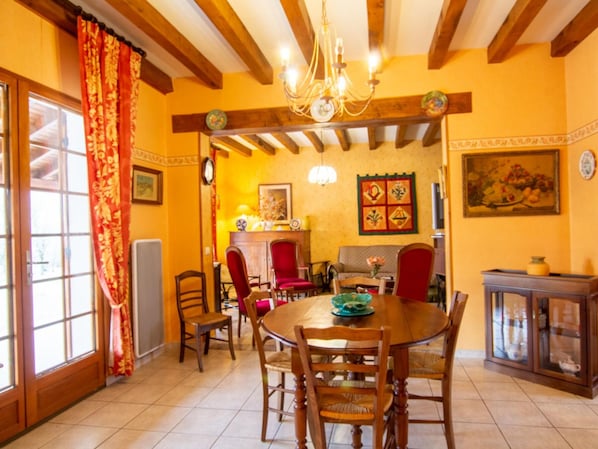A dining area with a wooden table, chairs, a chandelier, and a view of a kitchen.